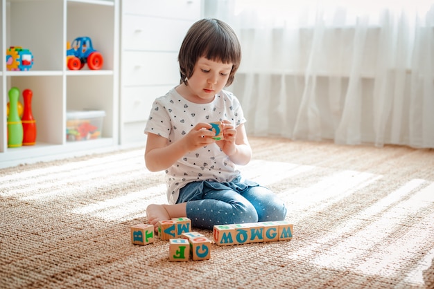 Giochi da bambini con i blocchi di legno con le lettere sull'asilo della casa della torre della costruzione della bambina della stanza del pavimento.