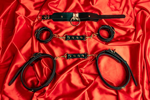 Giochi di sesso per adulti Articoli BDSM Cinturini in pelle manette e frusta su un lenzuolo di raso rosso