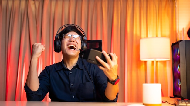 Giochi online di esportazione Giocatore asiatico felice ed eccitato che gioca online su smartphone Stanza colorata con luci al neon Gioco online di esportazione