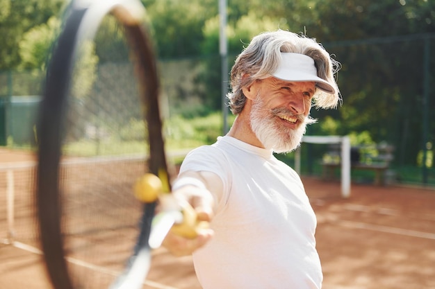 Gioco Senior uomo moderno ed elegante con racchetta all'aperto sul campo da tennis durante il giorno