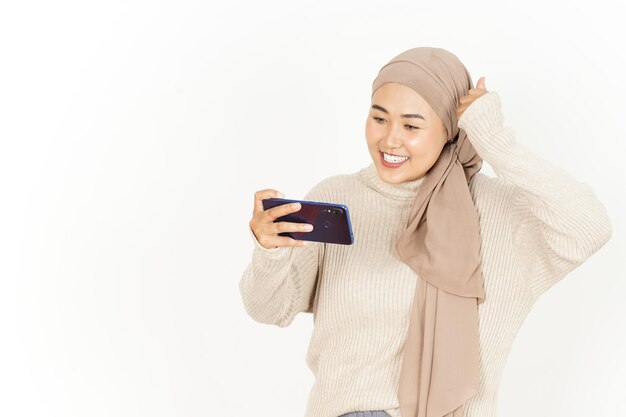 Gioco su smartphone di bella donna asiatica che indossa l'hijab isolato su sfondo bianco