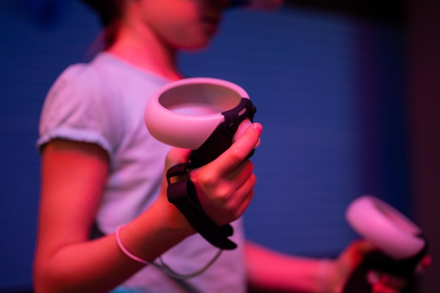 Gioco Vr e realtà virtuale kid girl gamer otto anni divertente giocando su un videogioco di simulazione futuristica tenendo in mano i joystick nell'intrattenimento vr room innovazione tecnologia e luce al neon