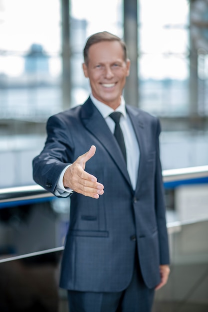 Gioia dell'incontro. Gioioso uomo affabile in abito formale scuro e cravatta che allunga la mano per la stretta di mano quando si incontra all'aeroporto