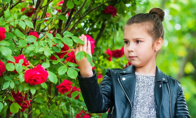 Gioia sincera. natura primaverile ed estiva. bambina in giardino. bambino godetevi il fiore nel parco. piccola signora carina in giacca di pelle. infanzia felice. bellezza e moda. bel bambino odore di fiori di rosa.