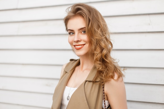 Gioiosa affascinante giovane donna con trucco naturale con capelli biondi ricci in un elegante giubbotto sorride