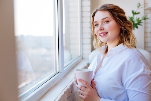 Gioiosa donna attraente di umore positivo mentre guarda nella finestra