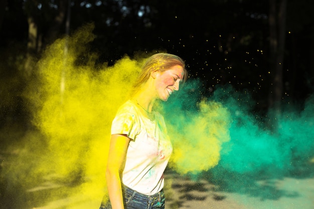 Gioiosa donna bionda che gioca con vernice secca gialla e verde Holi nel parco