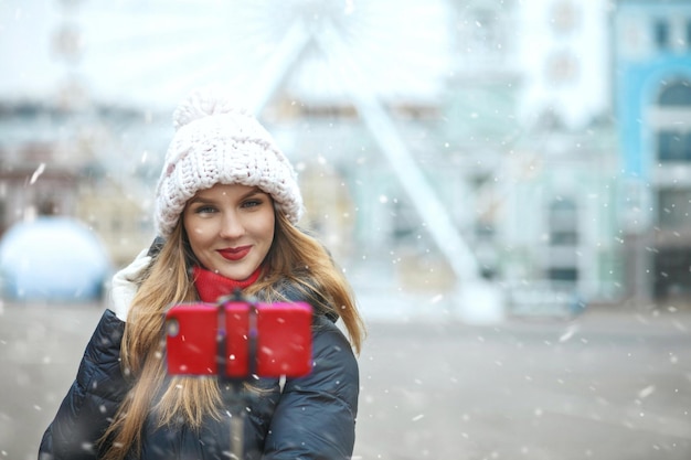 Gioiosa donna bionda con i capelli lunghi che si fa selfie in una piazza centrale della città durante la nevicata. Spazio vuoto