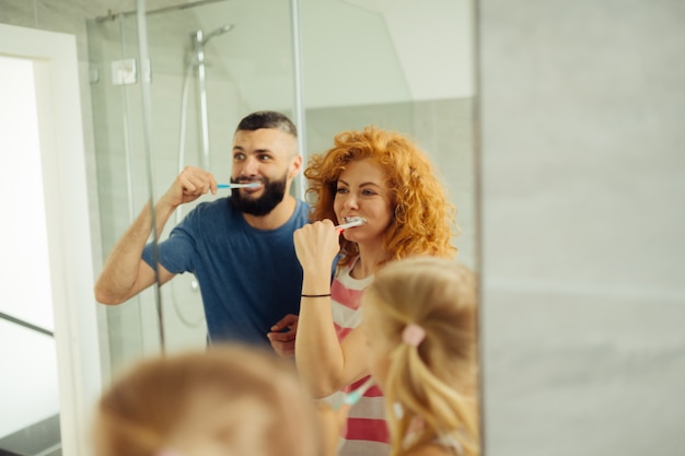 Gioiosa donna dai capelli rossi lavarsi i denti insieme alla famiglia