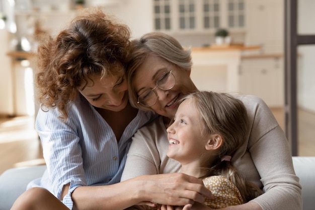 Gioiosa felice tre generazioni di donne famiglia bambina mamma adulta matura nonna abbraccio solletico risatina sul divano ridere divertirsi Amorevole madre nonna godere divertente gioco attivo con piccola figlia nipote