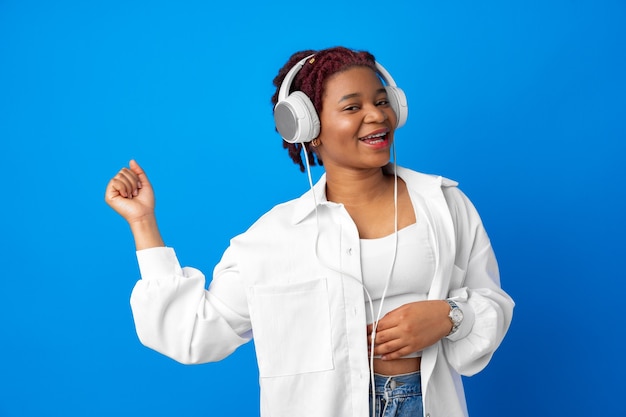 Gioiosa giovane donna afroamericana che ascolta musica con le cuffie su sfondo blu
