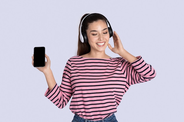 Gioiosa giovane donna che ascolta la musica in cuffia utilizzando lo smartphone