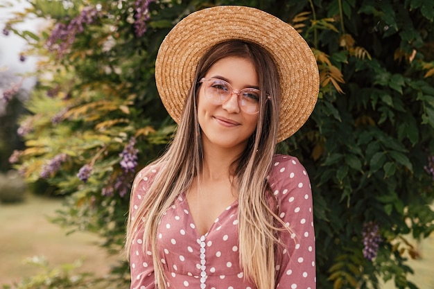 Gioiosa giovane donna con cappello e occhiali che riposano nel giardino estivo