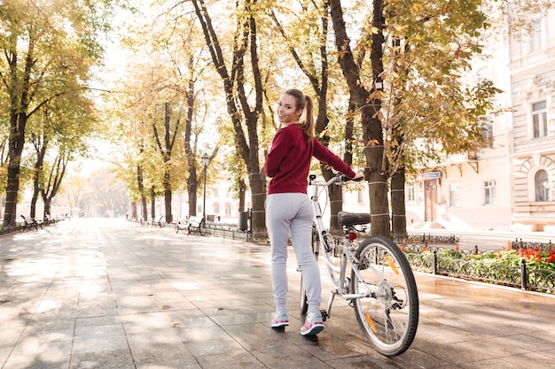 Gioiosa signora vestita di maglione che cammina con la sua bicicletta all'aperto