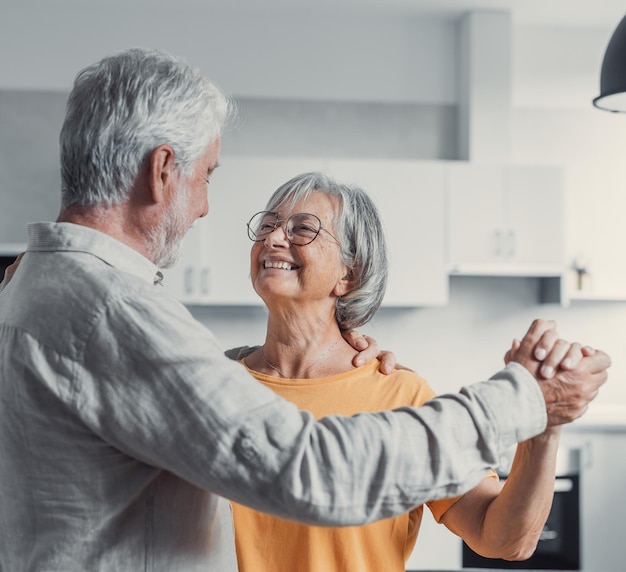 Gioiosa vecchia coppia romantica in pensione attiva che balla ridendo nel soggiorno felice moglie di mezza età e marito anziano che si divertono a casa sorridendo nonni anziani della famiglia rilassati che si legano insieme xA