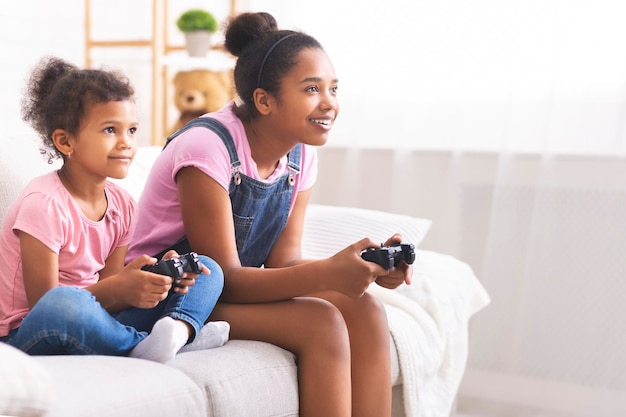 Gioiose sorelle afroamericane con joystick che giocano ai videogiochi