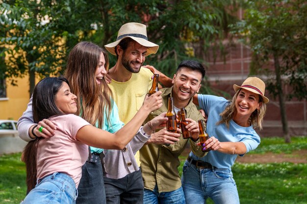 Gioiosi amici multiculturali abbracciano tostando birre colorate nella celebrazione del parco cittadino