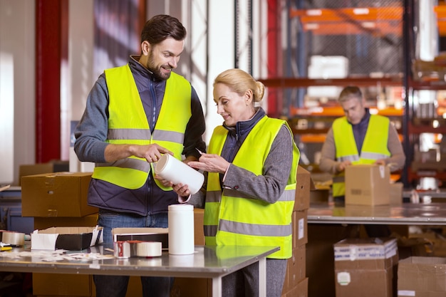 Gioiosi simpatici operai della manifattura che stanno insieme mentre fanno il lavoro in fabbrica