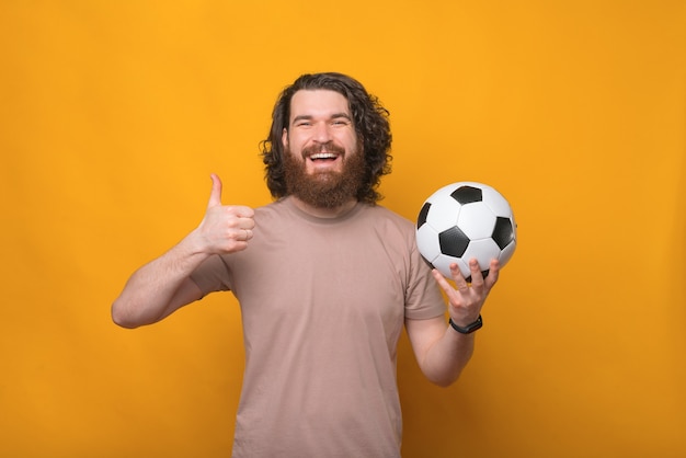 gioioso bell'uomo con i capelli lunghi tenendo il pallone da calcio e mostrando il pollice in alto gesto