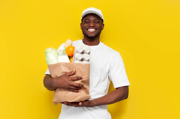 gioioso consegnatore afroamericano in uniforme bianco tiene l'ordine su uno sfondo giallo isolato