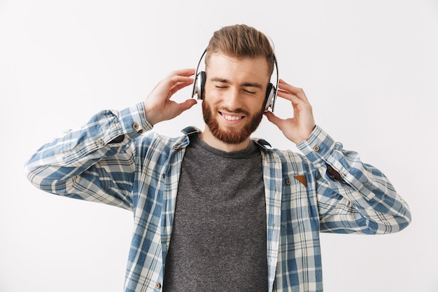 Gioioso uomo barbuto in camicia e cuffie che ascolta musica