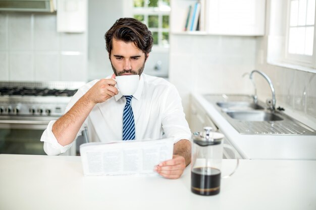 Giornale della lettura dell'uomo d'affari mentre bevendo caffè alla tavola