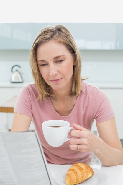 Giornale della lettura della donna mentre mangiando caffè in cucina