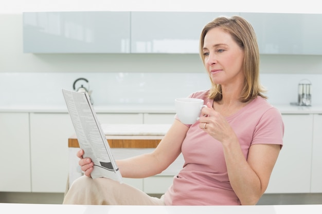 Giornale della lettura della donna mentre mangiando caffè in cucina