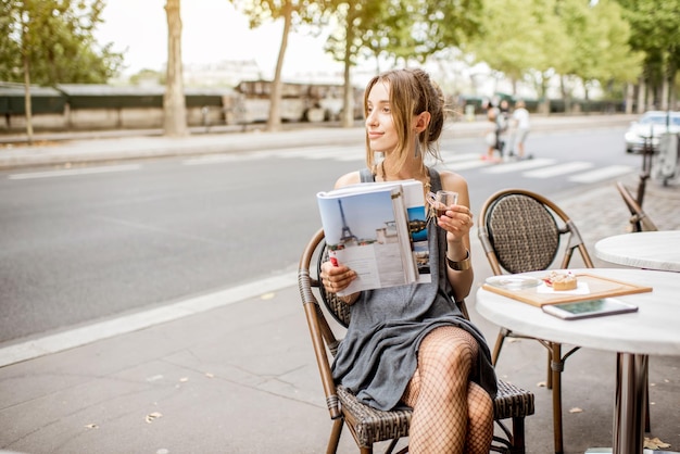 Giornale di lettura di giovane donna elegante seduto all'aperto al caffè di Paris