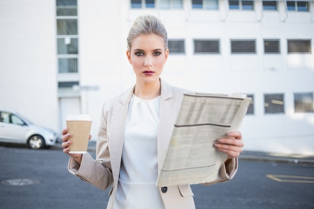 Giornale e caffè alla moda seri della tenuta della donna di affari