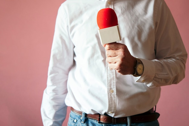 Giornalista con microfono in mano muro rosa
