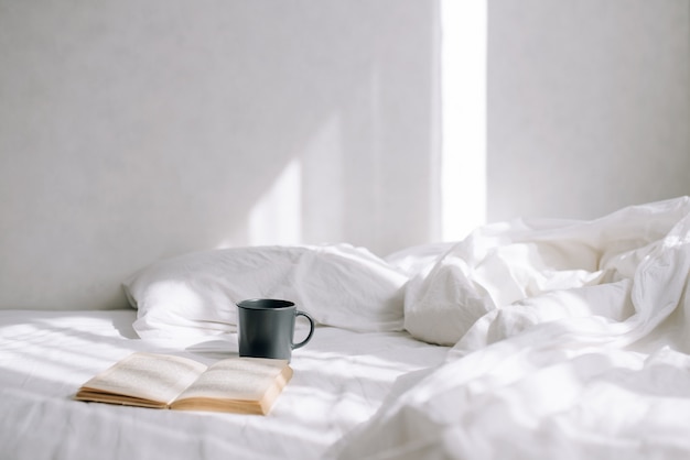 Giornata di sole in camera da letto luminosa. Sul letto c'è una tazza di caffè e un libro aperto. Bella mattina