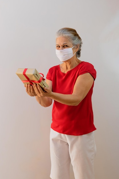 Giornata internazionale della donna Donna matura con maschera pandemica che tiene un regalo isolato su bianco