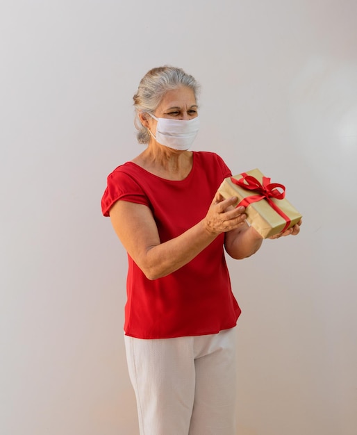 Giornata internazionale della donna Donna matura con maschera pandemica che tiene un regalo isolato su bianco