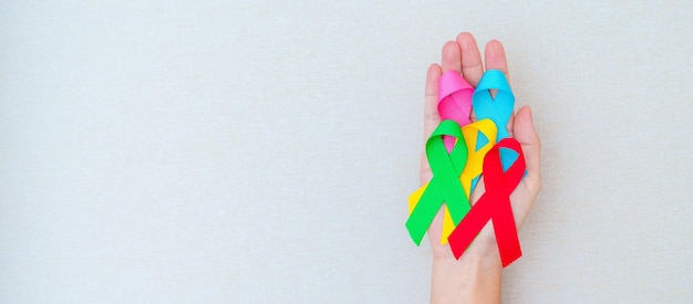 Giornata mondiale contro il cancro 4 febbraio Mano che tiene nastri blu rosso verde rosa e giallo per sostenere le persone che vivono e le malattie Concetto di giornata di sensibilizzazione sull'assistenza sanitaria e sull'autismo