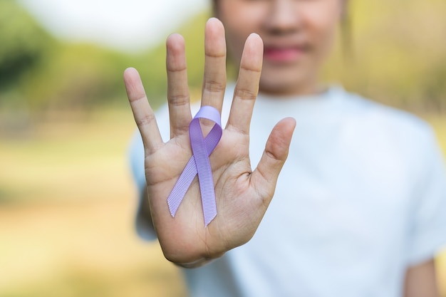 Giornata mondiale del cancro (4 febbraio). Mano della donna che tiene il nastro viola della lavanda per sostenere le persone che vivono e le malattie.