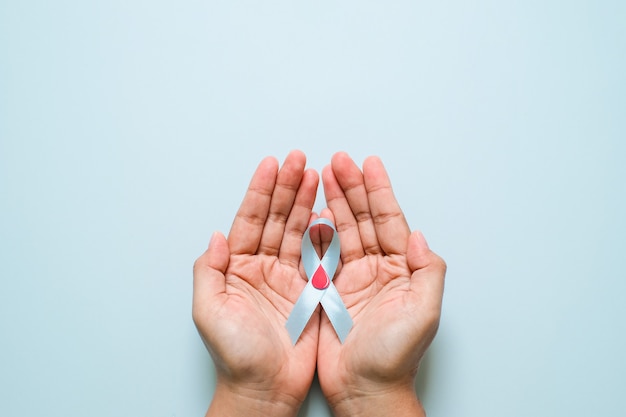 Giornata mondiale del diabete e consapevolezza del nastro blu con goccia di sangue rosso nelle mani della donna isolate su uno sfondo blu. Giornata mondiale del diabete, 14 novembre. Copia spazio. Vista dall'alto