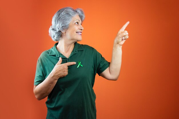 Giornata mondiale della salute mentale Donna matura con capelli grigi nastro verde e camicia isolata su arancione