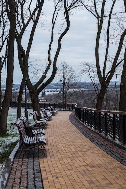 Giornata nuvolosa invernale nel parco cittadino. Vista sul fiume, panchine e neve leggera. Vista panoramica della città.