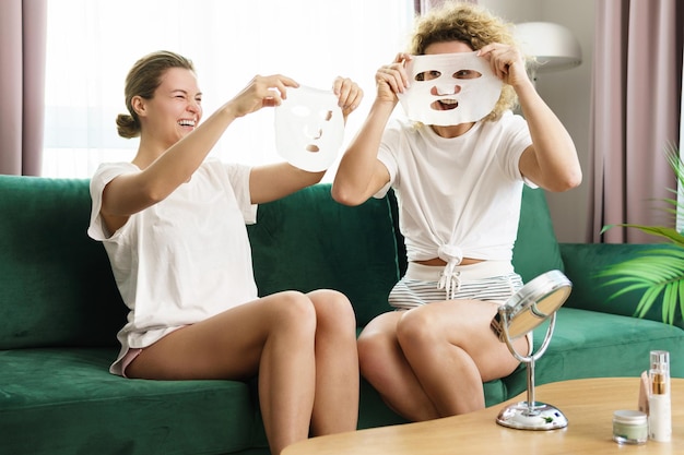 Giornata termale a casa. Due ragazze belle e allegre con una maschera in tessuto per l'idratazione della pelle.