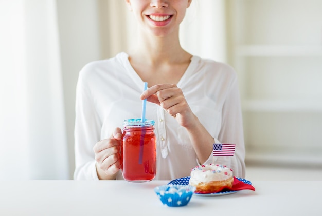 giorno dell'indipendenza, celebrazione, patriottismo e concetto di vacanze - primo piano di una donna felice che mangia una ciambella dolce smaltata, beve succo da un barattolo di vetro o una tazza e festeggia il 4 luglio a casa