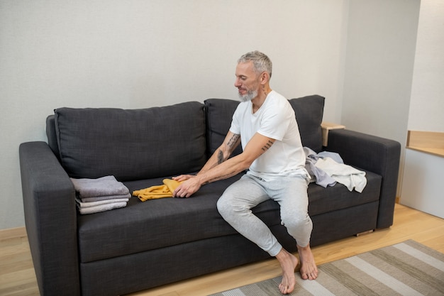 Giorno di bucato. Un uomo dai capelli grigi seduto sul divano e guardando i vestiti che giacciono vicino