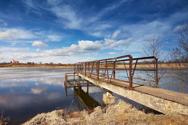 Giorno di primavera di marzo Scioglimento del ghiaccio e della neve sul lago Nubi riflesso nell'acqua Chiesa sulla collina sullo sfondo Tempo calmo Cambio di stagione