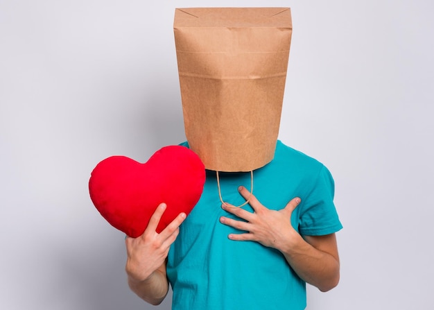 Giorno di San Valentino Teen ragazzo con sacchetto di carta sopra la testa detiene il cuore rosso Ragazzo che detiene il simbolo dell'amore