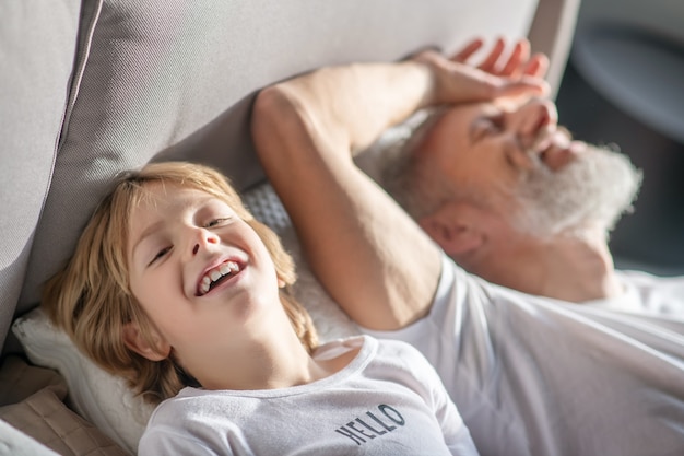 Giorno fortunato. Felice allegro bambino e papà in abiti domestici sdraiato sul letto a ridere