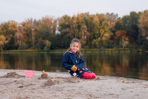 Giorno libero nella natura, la piccola ragazza felice sta giocando sulla riva del fiume e ammira la foresta autunnale con ...