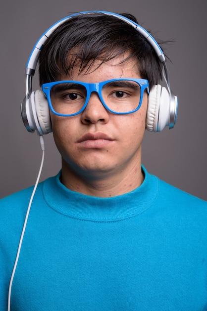 Giovane adolescente asiatico che ascolta la musica contro il backgrou grigio