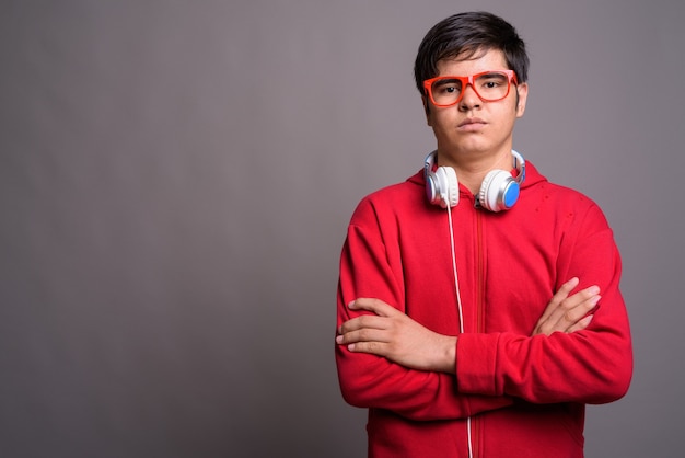 Giovane adolescente asiatico che indossa le cuffie contro il muro grigio