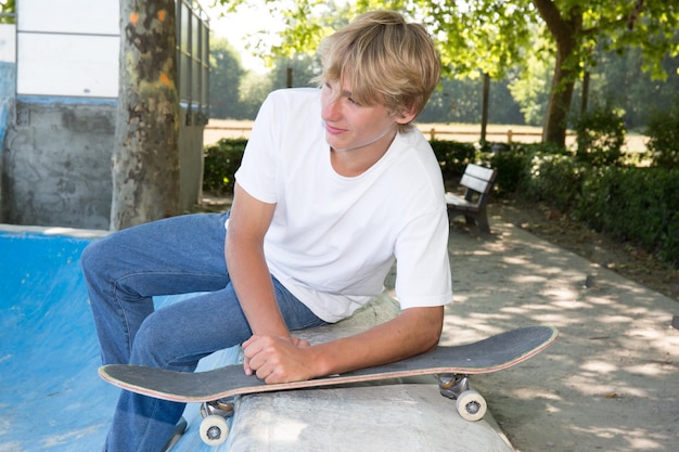 giovane adolescente biondo sta aspettando i suoi amici allo skatepark con la sua tavola