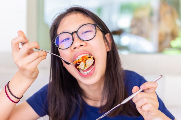 Giovane adolescente femminile con apparecchi ortodontici mangiare e mordere la sua pizza